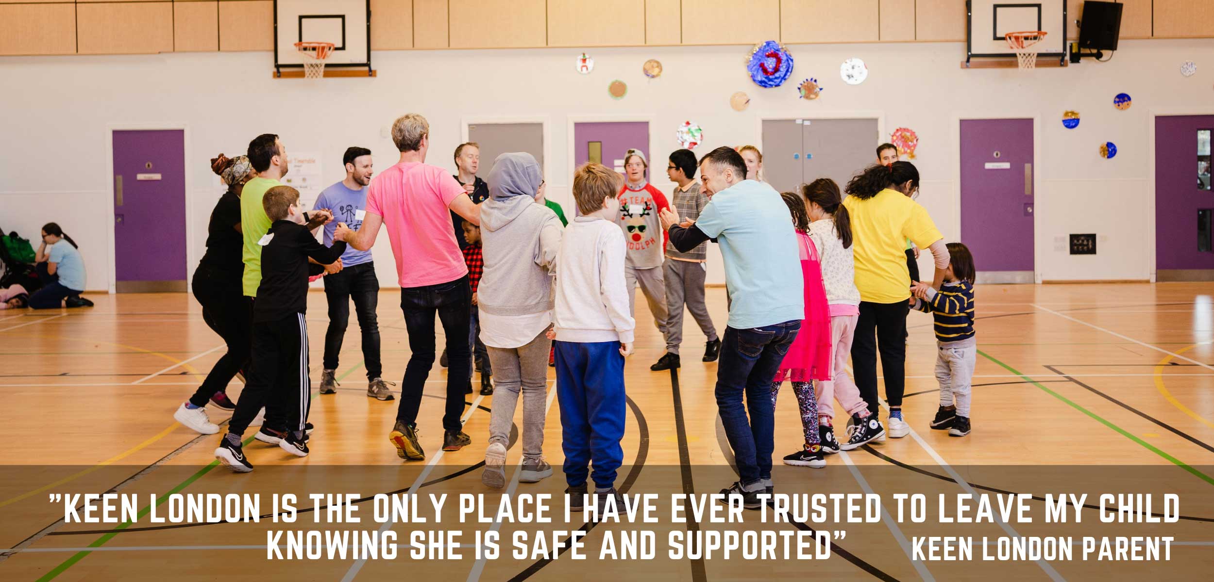 A supportive KEEN London volunteer assists a young girl in throwing a vibrant ball. 